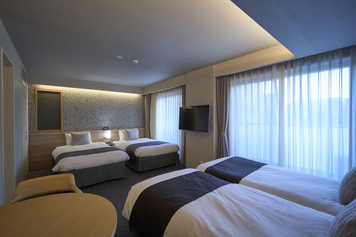 Une chambre d’hôtel avec deux lits, une télévision, une petite table et une fenêtre avec des rideaux.