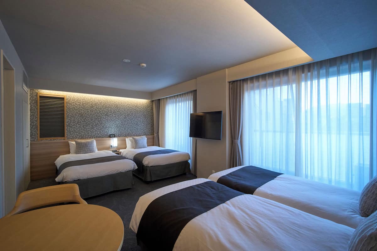 Une chambre d’hôtel avec deux lits, un téléviseur à écran plat et une grande fenêtre avec des rideaux.
