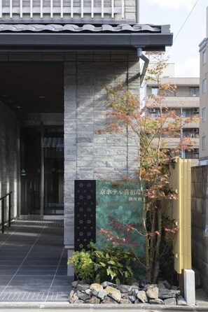 L’entrée d’un immeuble avec une façade en pierre, une enseigne et un petit arbre aux feuilles d’automne.