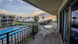Een balkon met een zwembad, stoelen en uitzicht op zee bij zonsondergang.