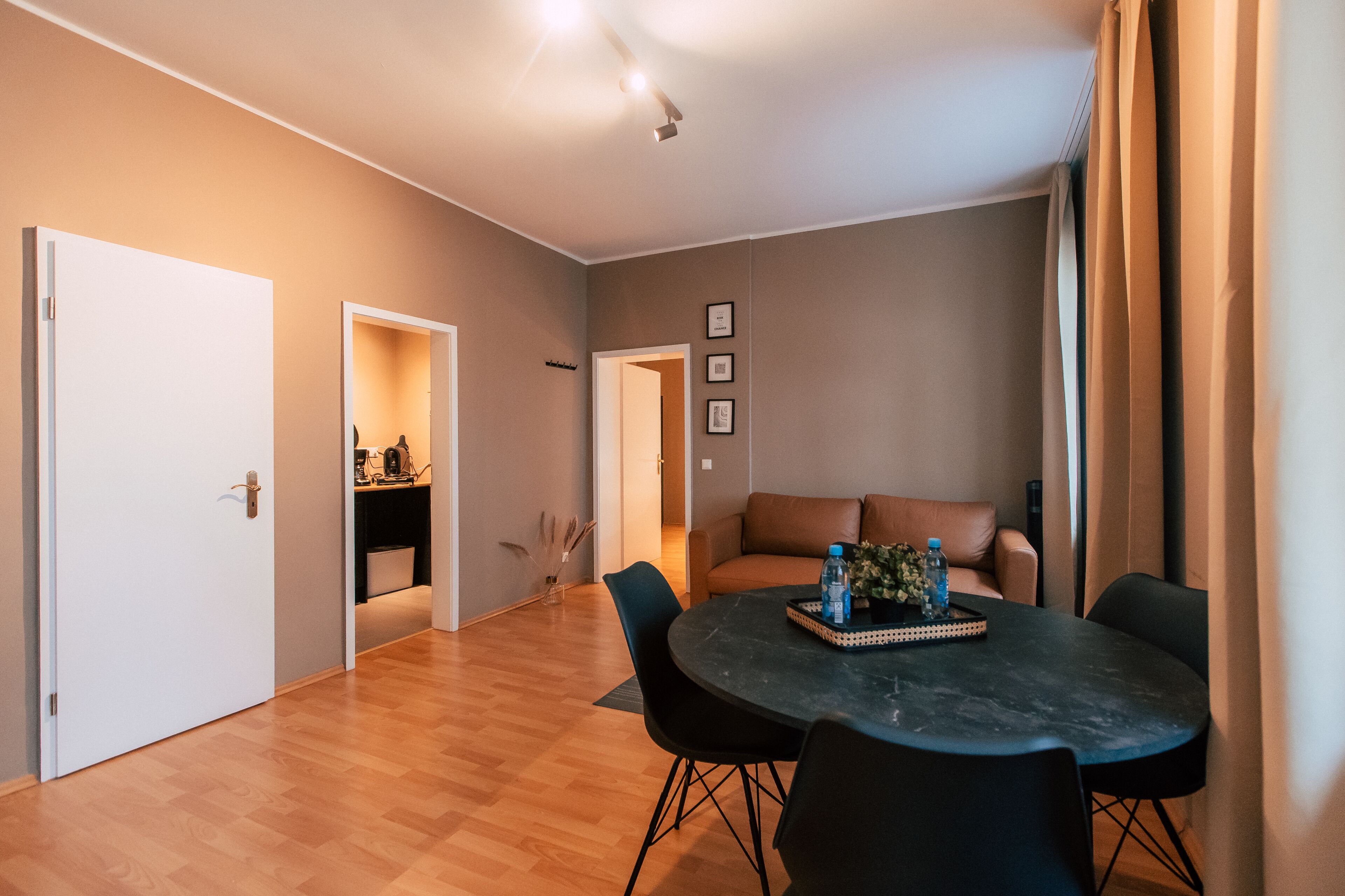 A modern living room with a round table, black chairs, a brown sofa, and a dining area.