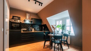 A modern kitchen with a black countertop, built-in oven, and a dining area with a round table and chairs. - Luga Homes - Chausseehaus (Leipzig)