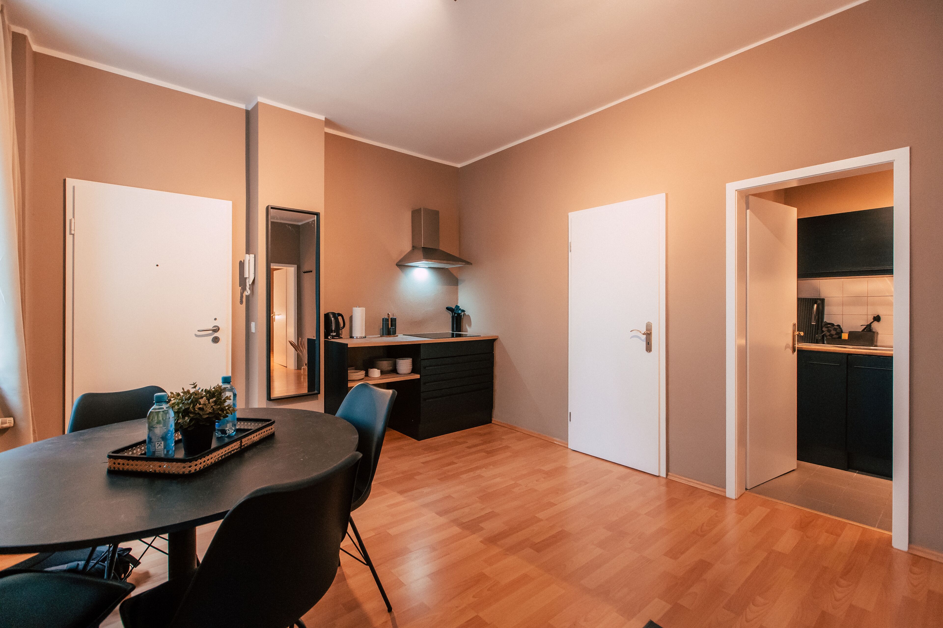 Een moderne keuken met een fornuis, spoelbak en kasten. Er is een eethoek met een tafel en stoelen.
