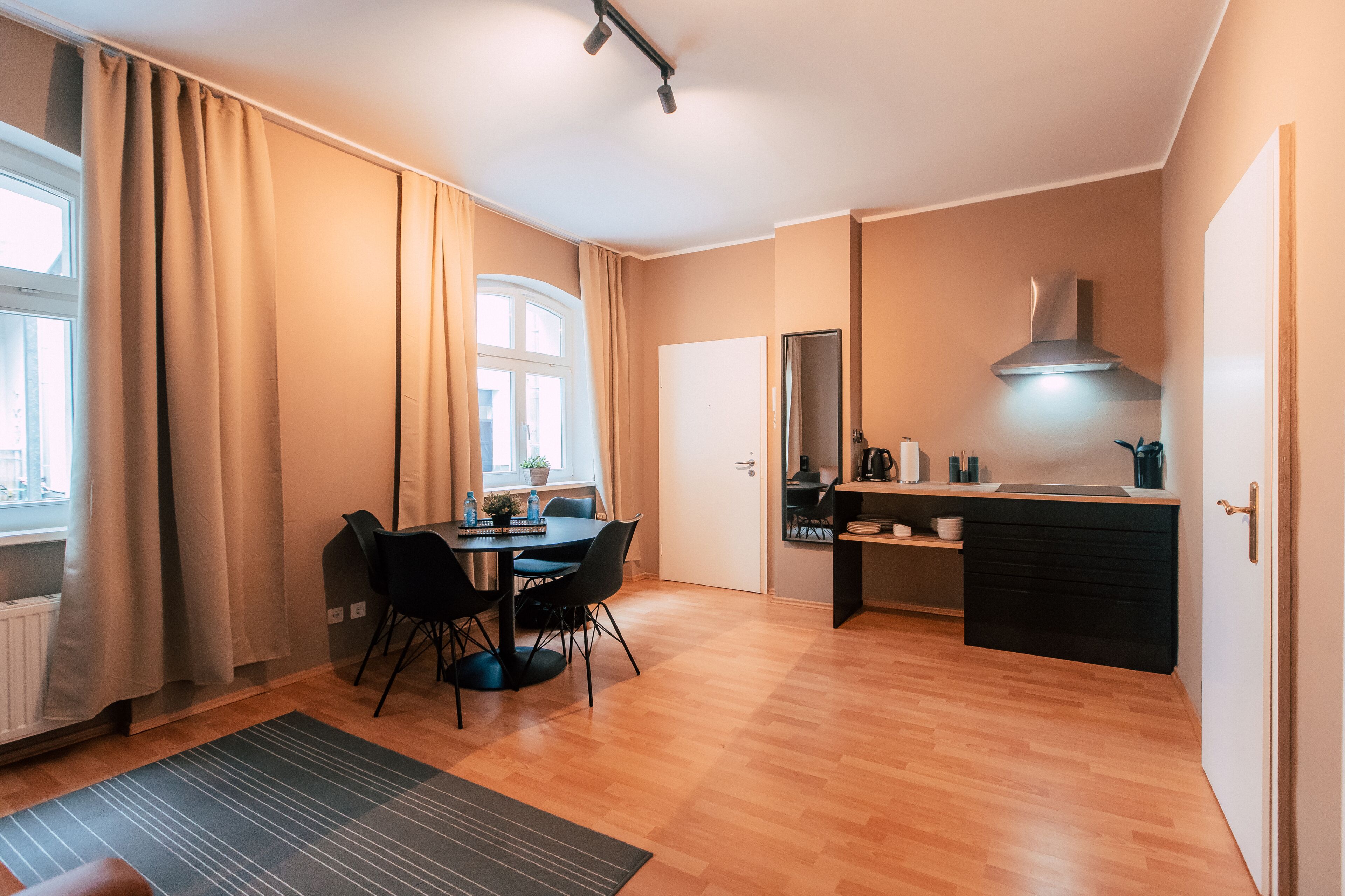 A modern kitchen with a black countertop, a stove, and a window with beige curtains.
