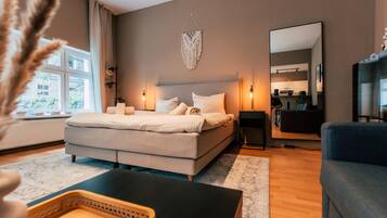 A modern bedroom with a large bed, bedside lamps, a mirror, and a view of the kitchen.