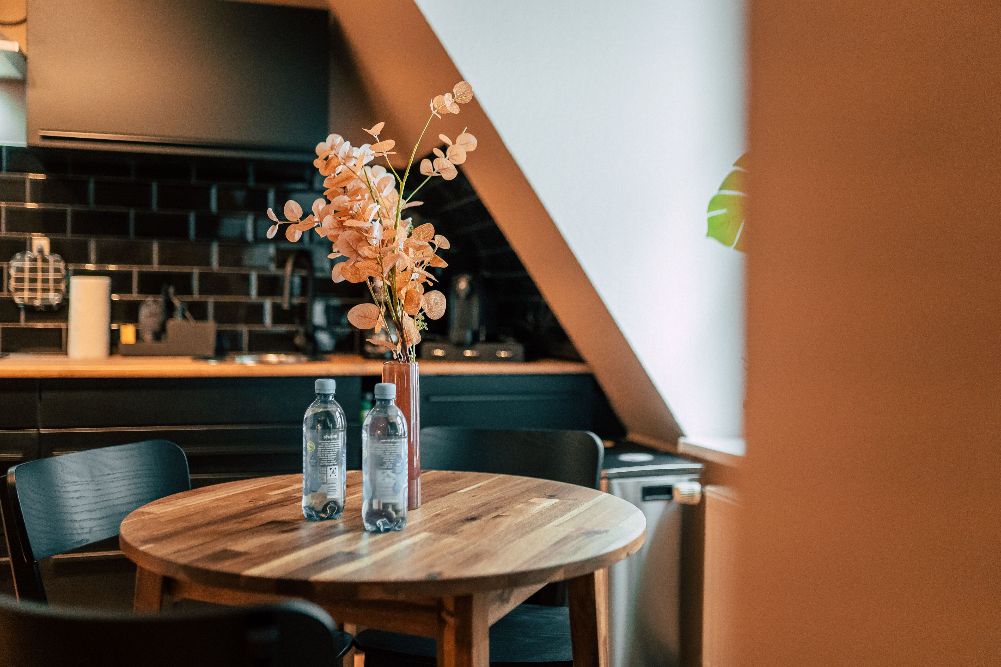 Een ronde houten tafel met twee waterflessen en een bloevas.