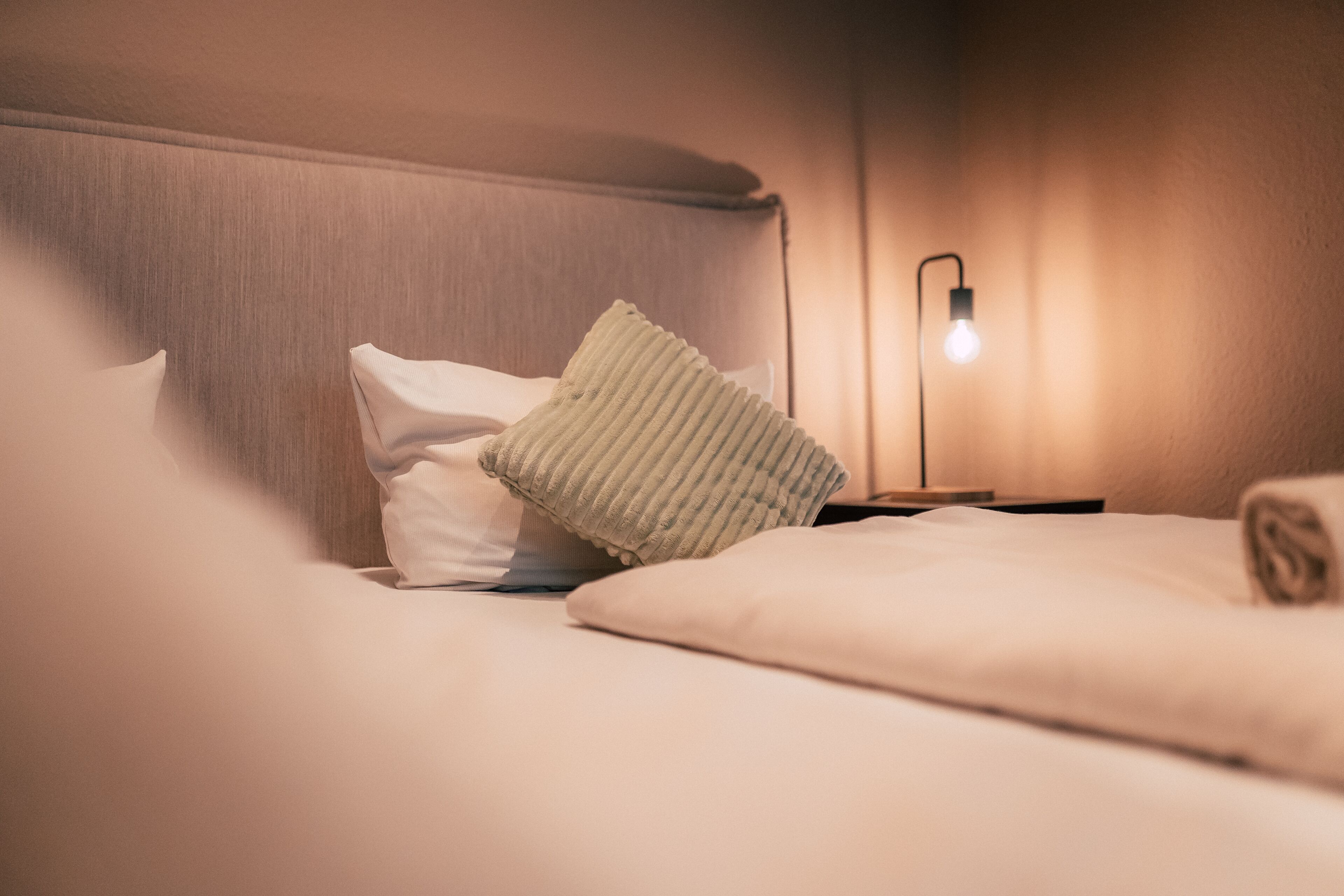 Ein ordentlich bezogenes Bett mit Kissen und einer Nachttischlampe.