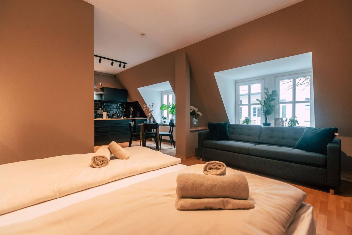A modern bedroom with two beds, a sofa, and a dining area.