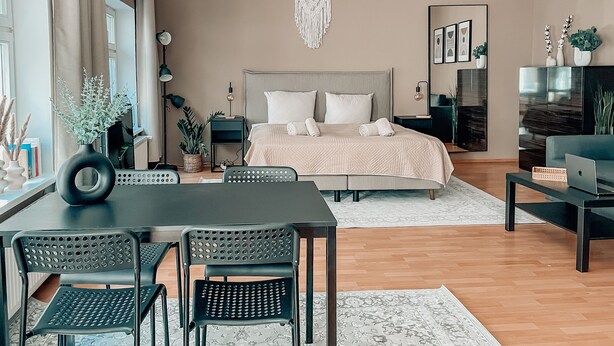 A modern bedroom with a large bed, bedside tables, a desk, and chairs. - Luga Homes - Chausseehaus (Leipzig)