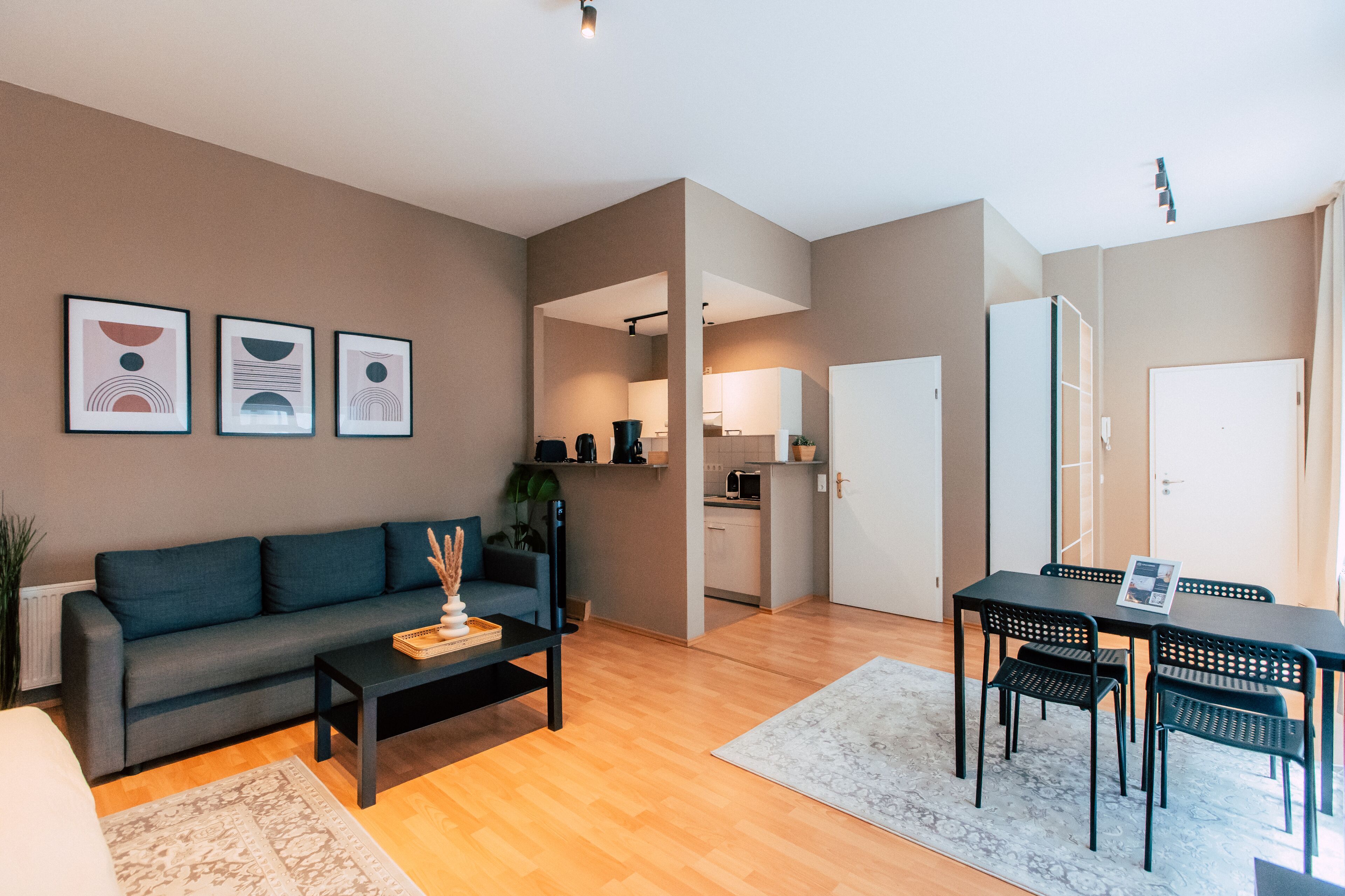 Ein modernes Wohnzimmer mit einer Couch, einem Couchtisch und einem Essbereich mit Stühlen. Im Hintergrund befindet sich eine Küche.