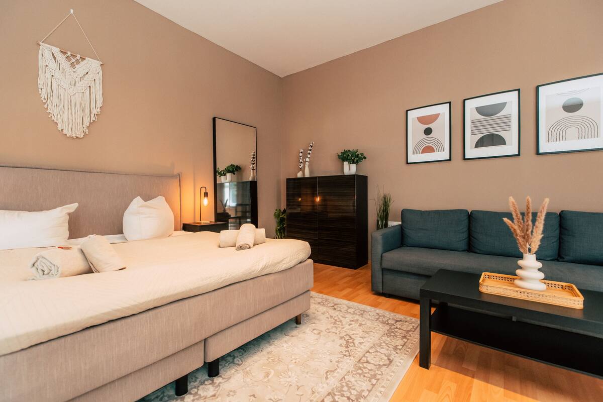 A modern bedroom with a bed, a dark wooden dresser, a grey sofa, and a black coffee table.