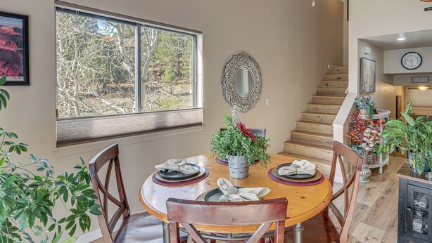 A dining area with a round table, chairs, a window with a view, a staircase, and a clock on the wall.