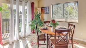 A dining area with a table, chairs, a potted plant, and a window with a view of trees.