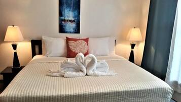 Un cuarto de hotel con una cama bien hecha, dos lámparas de noche, un cuadro en la pared y una ventana con cortinas.