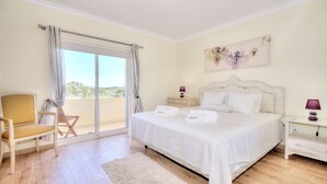 Un dormitorio con una cama grande, una silla, una mesita de noche y vistas a través de una puerta corredera.