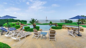 Área da piscina com espreguiçadeiras, guarda-sóis e vista para o mar e o cais.