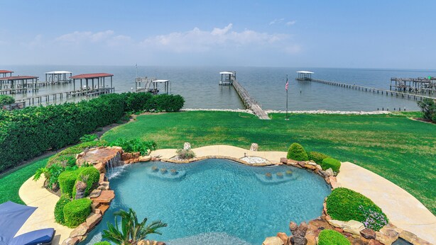 Piscina privativa com vista para o oceano, rodeada por paisagismo bem cuidado e um píer que se estende para a água.