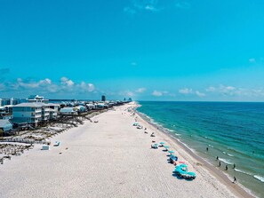 A beach with a long stretch of sand, a few umbrellas, and buildings along the shore. - Escape to Sun Dreams 1 Your Perfect Gulf Shores Getaway Direct Gulf Front by Prickett Properties (Gulf Shores)