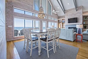 A spacious living area with a large dining table, white chairs, a chandelier, and a television mounted on the wall. - Escape to Sun Dreams 1 Your Perfect Gulf Shores Getaway Direct Gulf Front by Prickett Properties (Gulf Shores)