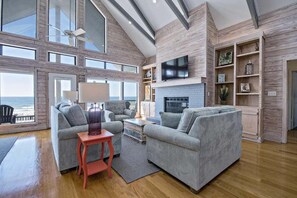 A spacious living room with a large window overlooking the ocean, a fireplace, and a television mounted on the wall. - Escape to Sun Dreams 1 Your Perfect Gulf Shores Getaway Direct Gulf Front by Prickett Properties (Gulf Shores)