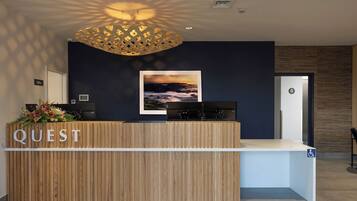 A reception desk with a wooden finish, a sign reading "QUEST," and a framed landscape painting above it.