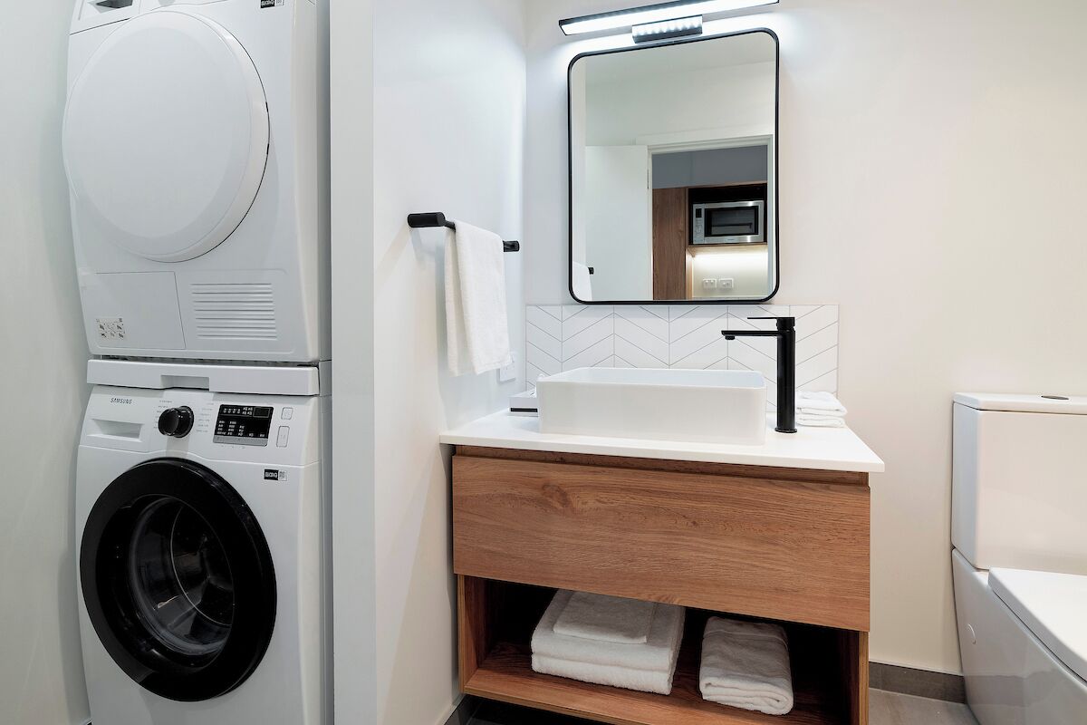 A modern bathroom with a built-in washer and dryer, a wooden vanity with a mirror, and a white sink.