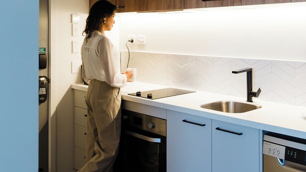 Una cocina moderna con armarios blancos, un muro decorativo de madera, un lavamanos de acero inoxidable y un lavavajillas.