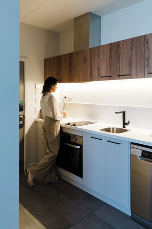 A modern kitchen with white cabinets, a wooden accent wall, a stainless steel sink, and a dishwasher. - Quest Hastings (Hastings)