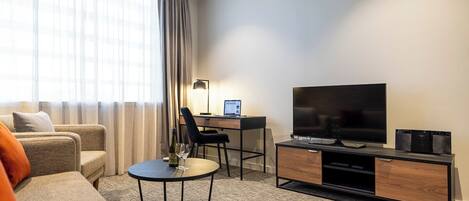 Una habitación de hotel moderna con sofá, escritorio, ordenador portátil, televisor y mesa de centro.