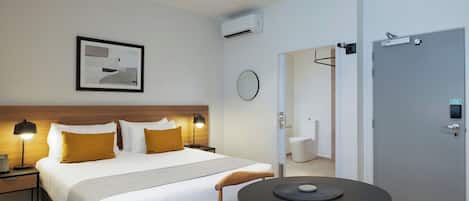 Een hotelkamer met een bed, bedlampjes, een ronde tafel met stoelen, een deur en een lijst aan de muur.