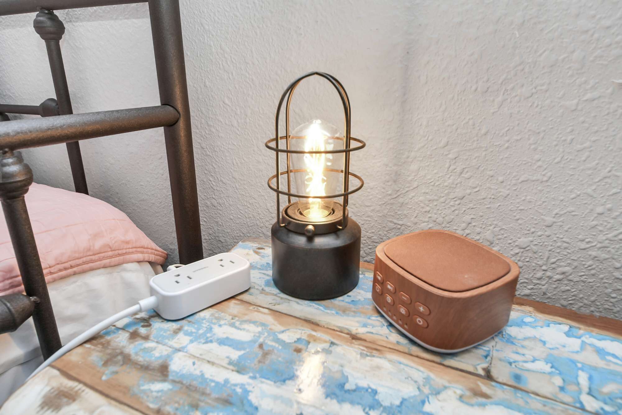 A bedside table with a power strip, a lantern, and a speaker.