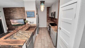 Una cocina estrecha con salpicadero de madera, un lámpara colgante y una puerta a la derecha.