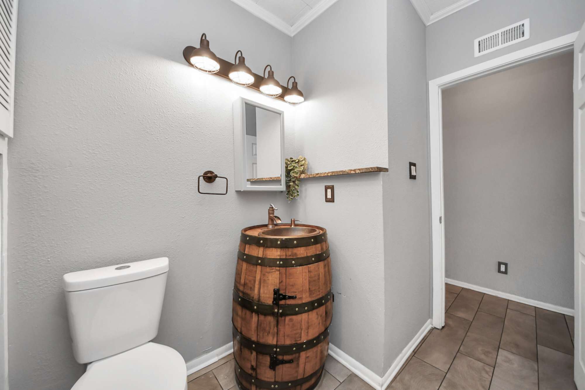Un baño con inodoro, lavamanos de barril de madera, espejo y lámpara sobre el espejo.