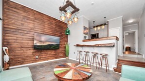 Una sala moderna con una pared de madera, una mesa colorida y una zona de cocina con taburetes.