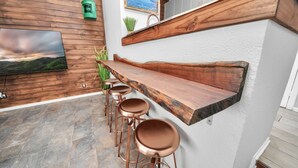 Una zona de bar con mostrador de madera, taburetes de cobre y una televisión en la pared.