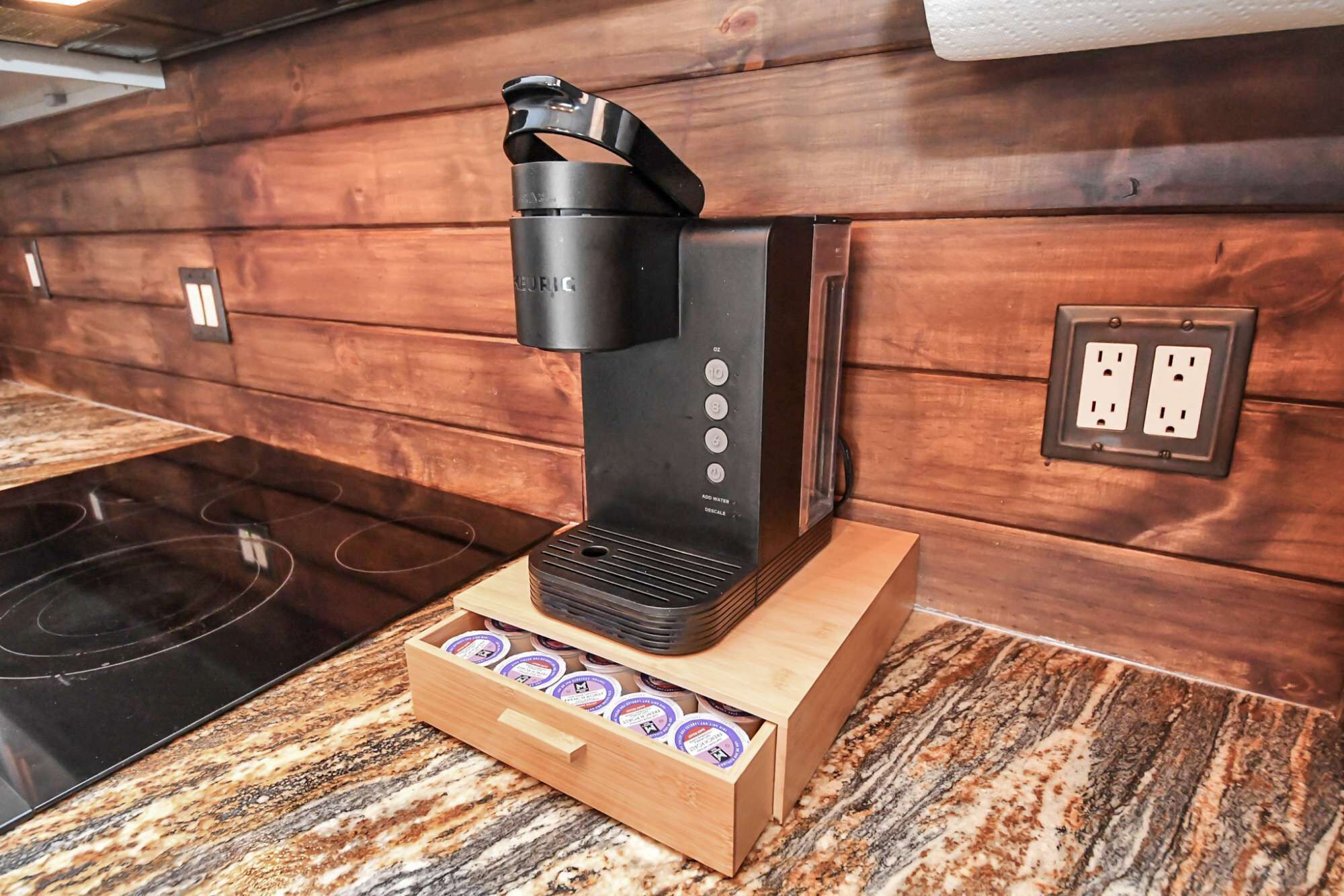 Una cafetera sobre una encimera de madera con un cajón de cápsulas de café.