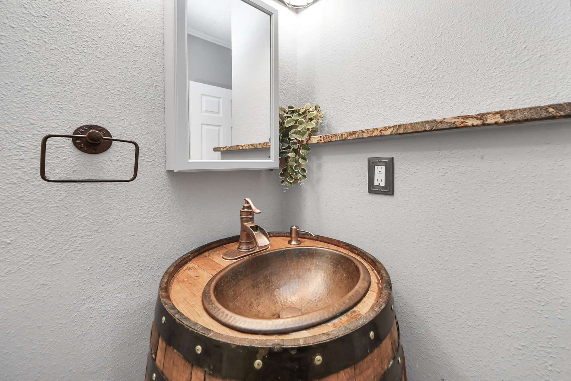 Une salle de bain avec un lavabo en forme de tonneau en bois, un miroir, une petite étagère avec une plante et une porte.
