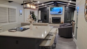 A modern kitchen with a large island, dining area, and a fireplace. - Stunning and Completely Remodeled Ranch Home! Walk to Downtown & Marina! (Port Washington)