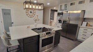 A modern kitchen with a central island, stainless steel appliances, and a clock on the wall. - Stunning and Completely Remodeled Ranch Home! Walk to Downtown & Marina! (Port Washington)