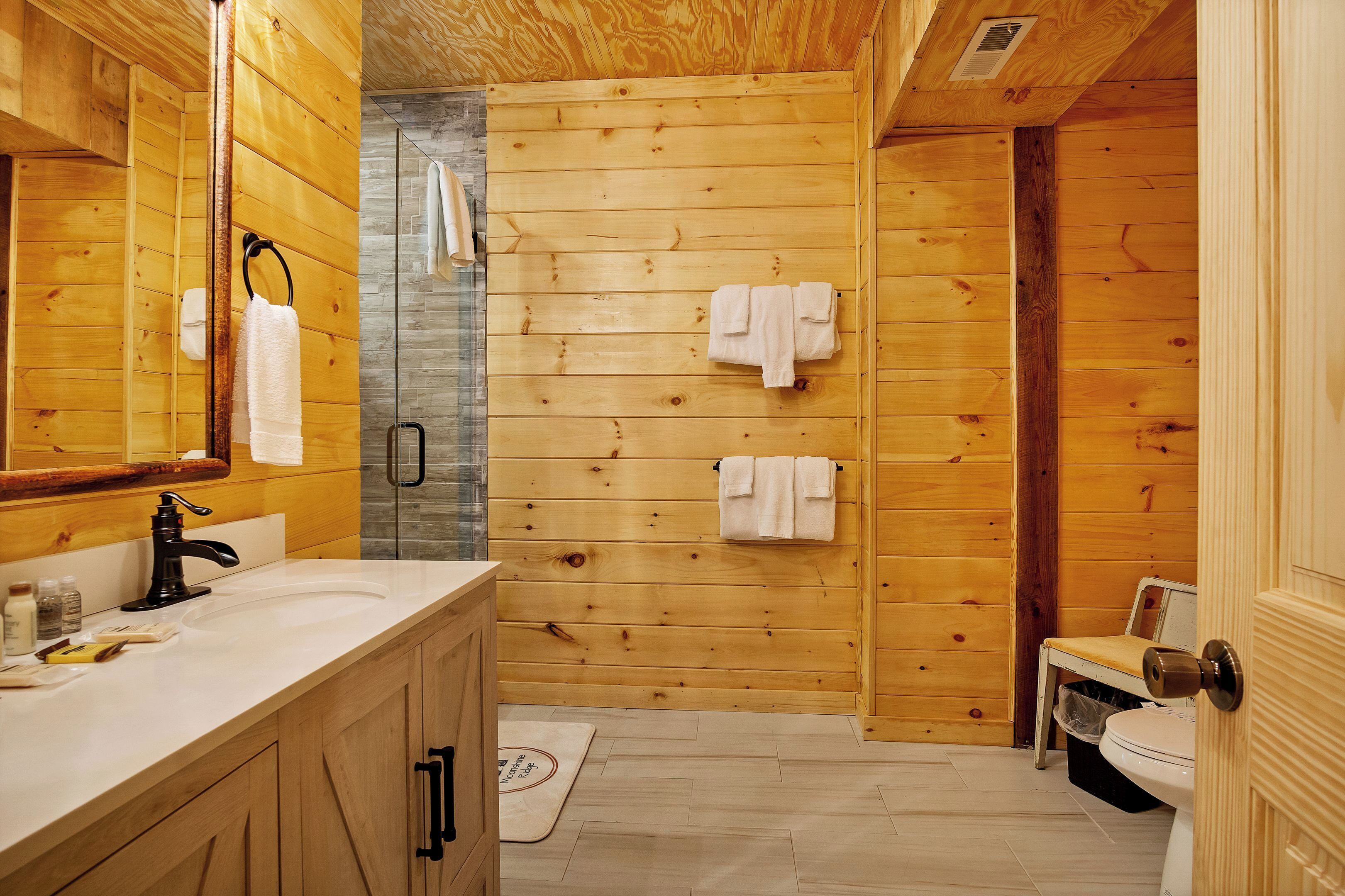 Een badkamer met houten lambrisering, een wastafel, spiegel, handdoekhouder en douche.