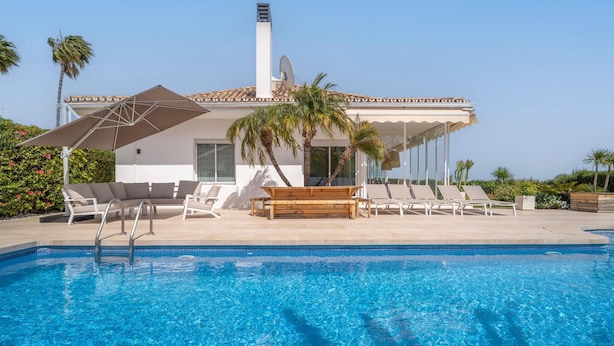 A poolside area with a clear blue pool, lounge chairs, a wooden bench, and palm trees. - Gorgeous home in Marbella (Marbella)