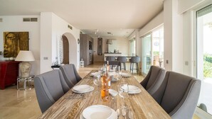 A dining area with a long wooden table set for six, grey upholstered chairs, and a view of the kitchen and dining area in the background. - Gorgeous home in Marbella (Marbella)