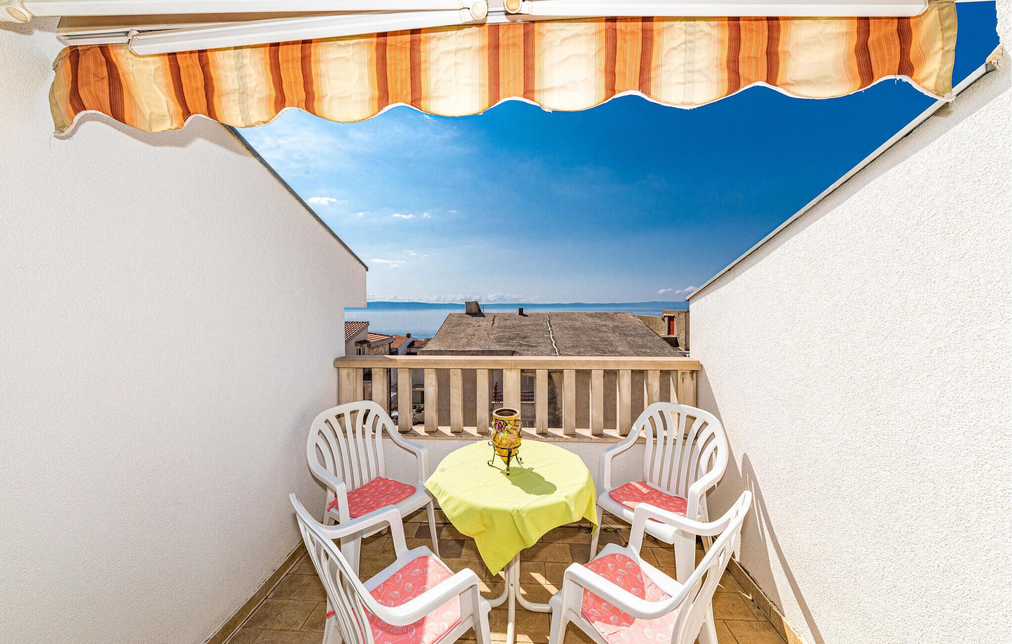 A small outdoor balcony with a table and chairs, a view of the sea, and a wooden railing.