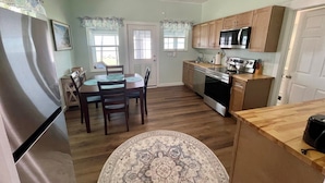 A kitchen with wooden cabinets, a stainless steel refrigerator, a microwave, and a stove. There is a dining table with chairs and a rug. - Aunt May's - Waterfront Cottage in Cedar Key! (Cedar Key)