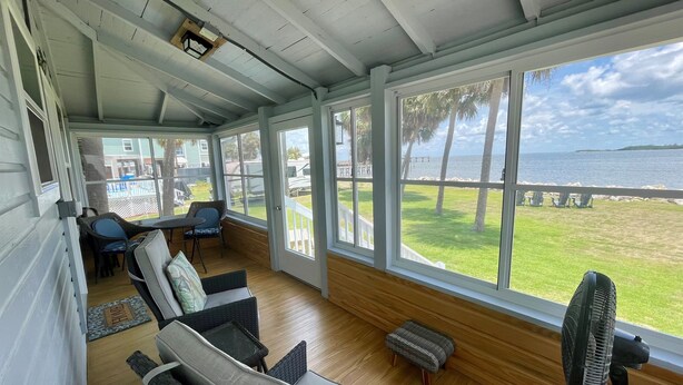 A covered outdoor seating area with wicker furniture, a fan, and a view of the beach and ocean. - Aunt May's - Waterfront Cottage in Cedar Key! (Cedar Key)