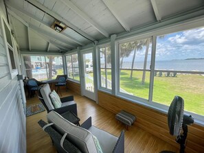 A covered outdoor seating area with wicker furniture, a fan, and a view of the beach and ocean. - Aunt May's - Waterfront Cottage in Cedar Key! (Cedar Key)