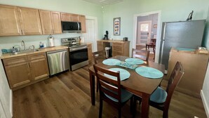 A kitchen with wooden cabinets, stainless steel appliances, a dining table with placemats, and a ceiling fan. - Aunt May's - Waterfront Cottage in Cedar Key! (Cedar Key)