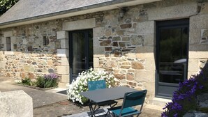 A stone building with a patio area featuring a table and chairs, a flower arrangement, and a stone wall. - Ty Rozenn Gwenn - PLOUGUIEL (PLOUGUIEL)