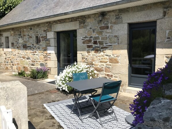 A stone building with a patio area featuring a table and chairs, a flower arrangement, and a stone wall.