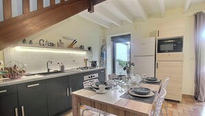 A modern kitchen with dark cabinets, a wooden dining table set for four, and a built-in microwave. - Ty Rozenn Gwenn - PLOUGUIEL (PLOUGUIEL)